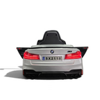 Vue arrière de la voiture électrique enfant Odecare BMW M5 24V gris métallisé avec feux allumés dans un showroom