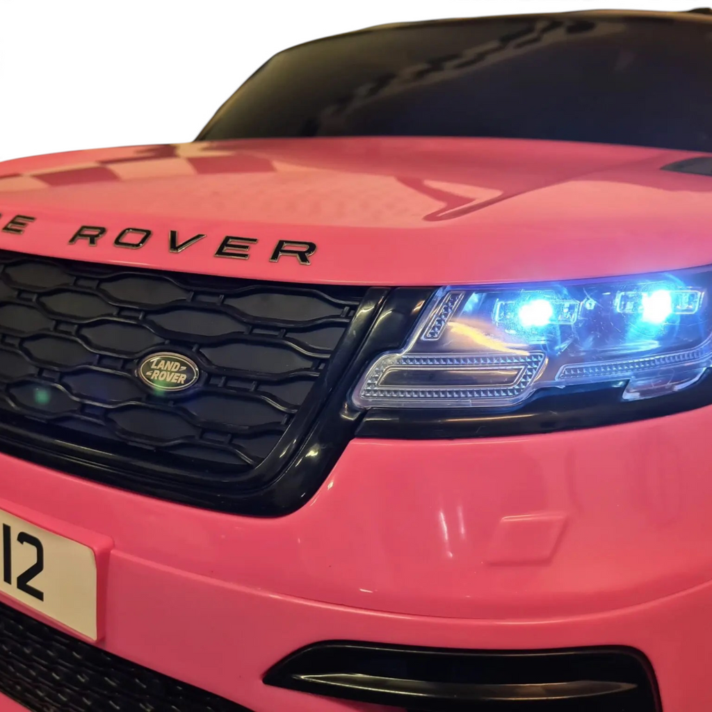 Gros plan sur la face avant rose de la voiture électrique pour enfant Petit Pilote Range Rover Velar avec phares LED allumés